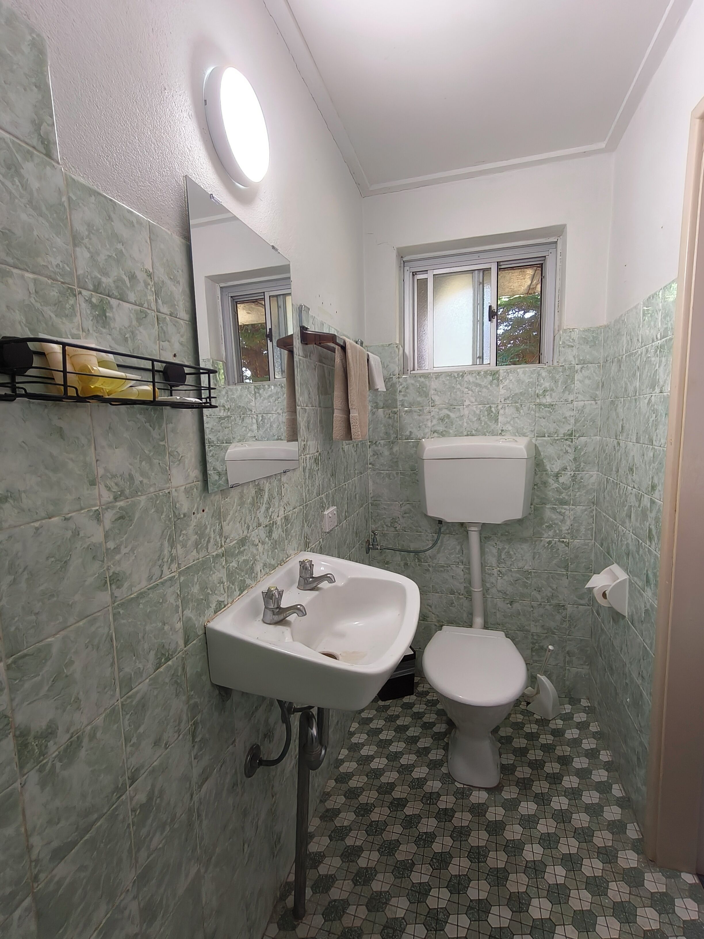 Een badkamer met een witte wastafel, toilet en een raam boven het toilet.