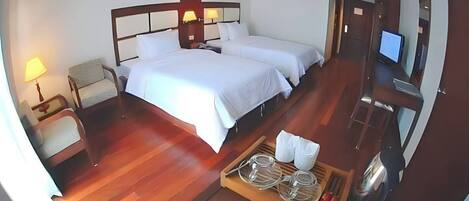 Une chambre d’hôtel avec un grand lit, deux tables de chevet avec des lampes, une télévision et un plateau avec des verres et une bouteille.