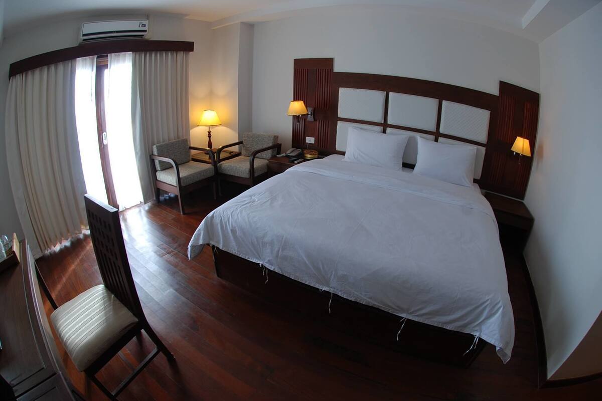 A hotel room with a large bed, two bedside lamps, a desk with a chair, and a window with curtains.