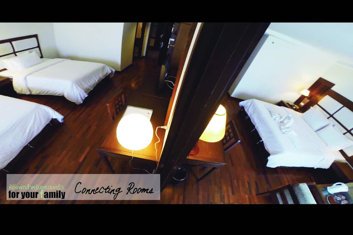 A hotel room with two single beds, a wooden floor, a table with a lamp, and a small desk with a chair.
