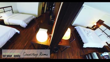 A hotel room with two single beds, a wooden floor, a table with a lamp, and a small desk with a chair.