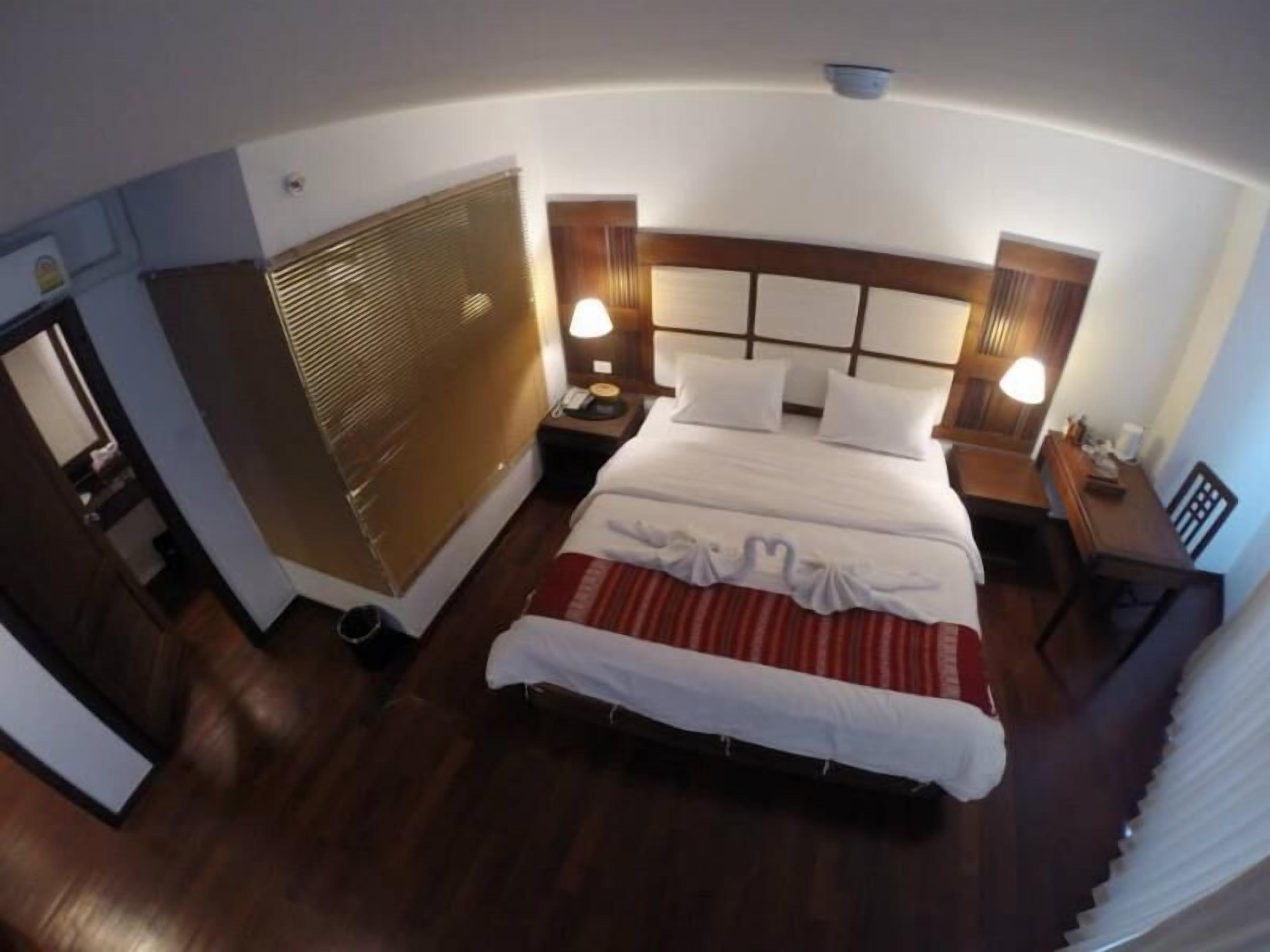 Quarto de hotel com uma cama grande, duas mesas de cabeceira, um painel de madeira na cabeceira e uma janela com persianas.