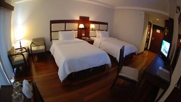 A hotel room with two beds, a TV, a desk with a lamp, and a chair.