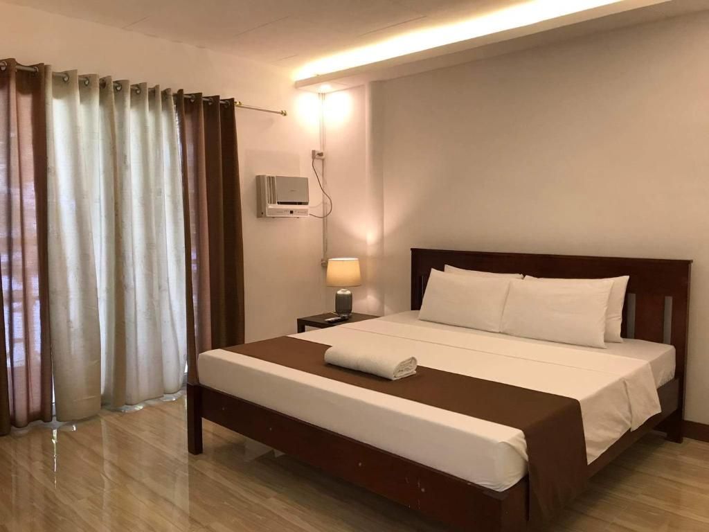A hotel room with a large bed, a bedside table with a lamp, and a wall-mounted air conditioning unit.