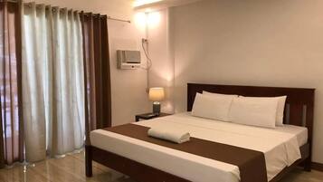 A hotel room with a large bed, a bedside table with a lamp, and a wall-mounted air conditioning unit.