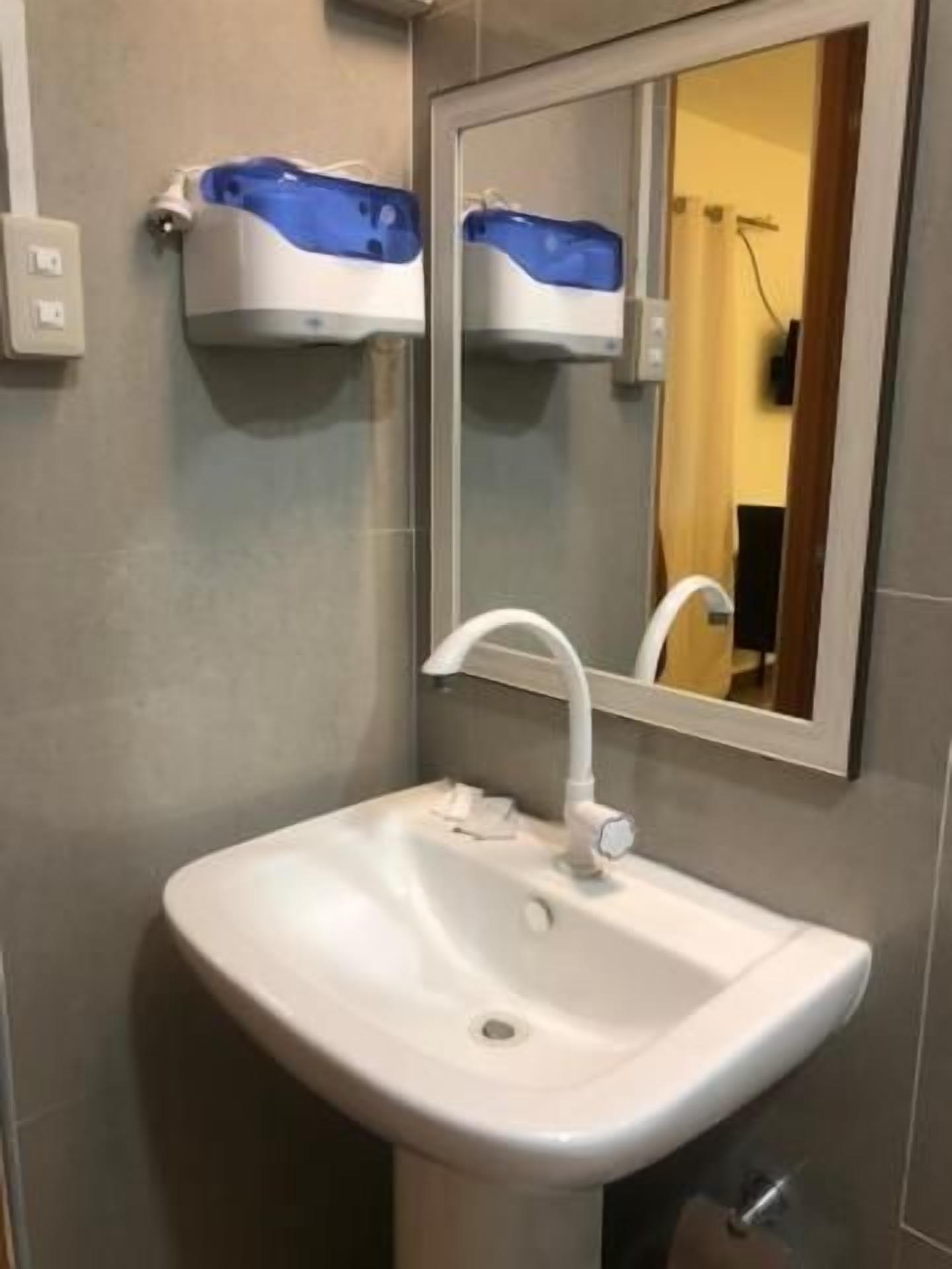 Un baño con un lavamanos blanco, un espejo y un dispensador de jabón azul en una repisa.