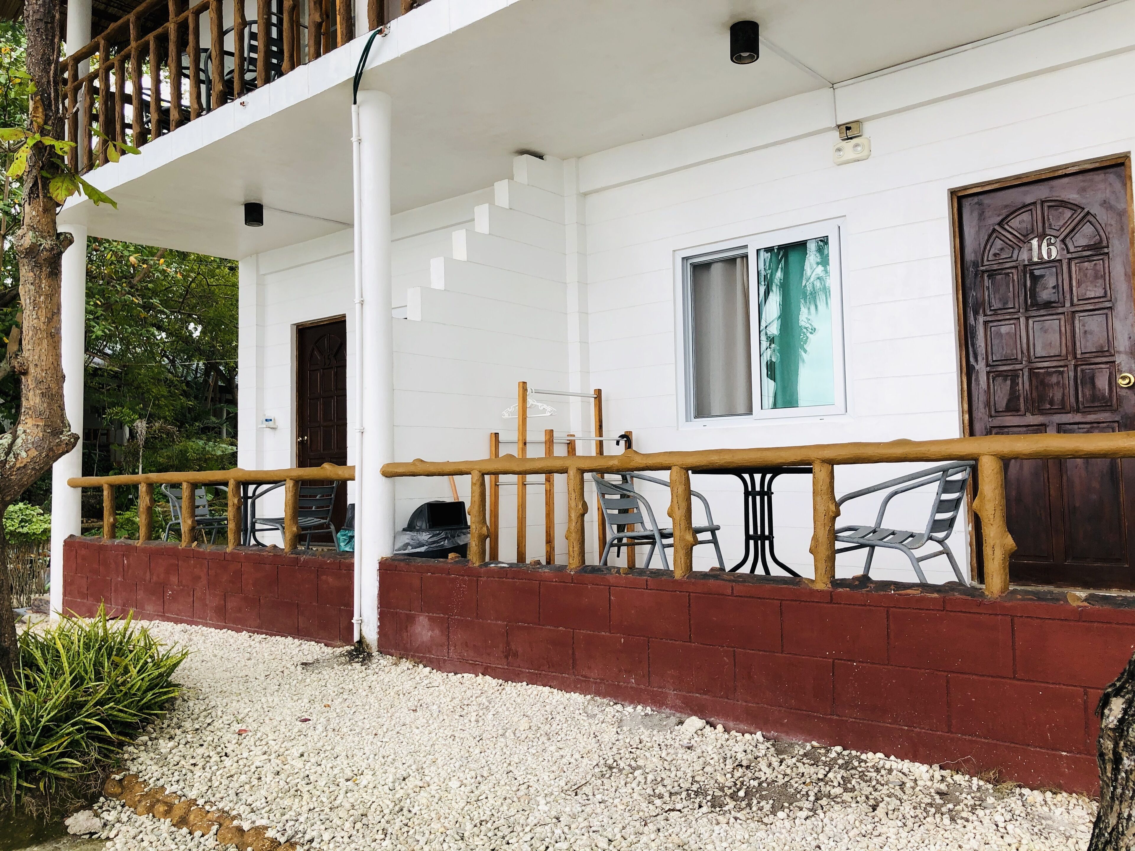 A white building with a wooden balcony, a window with a curtain, and a door marked with the number 16.