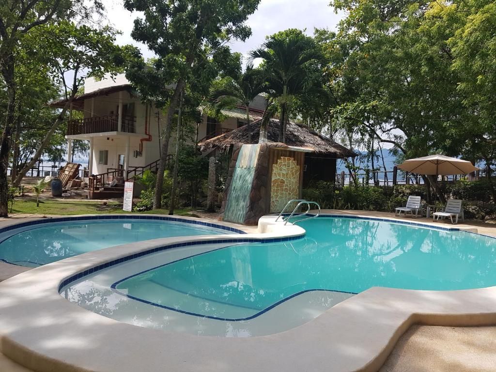 Una piscina amb cascada, envoltada d'arbres i un edifici amb balcó.