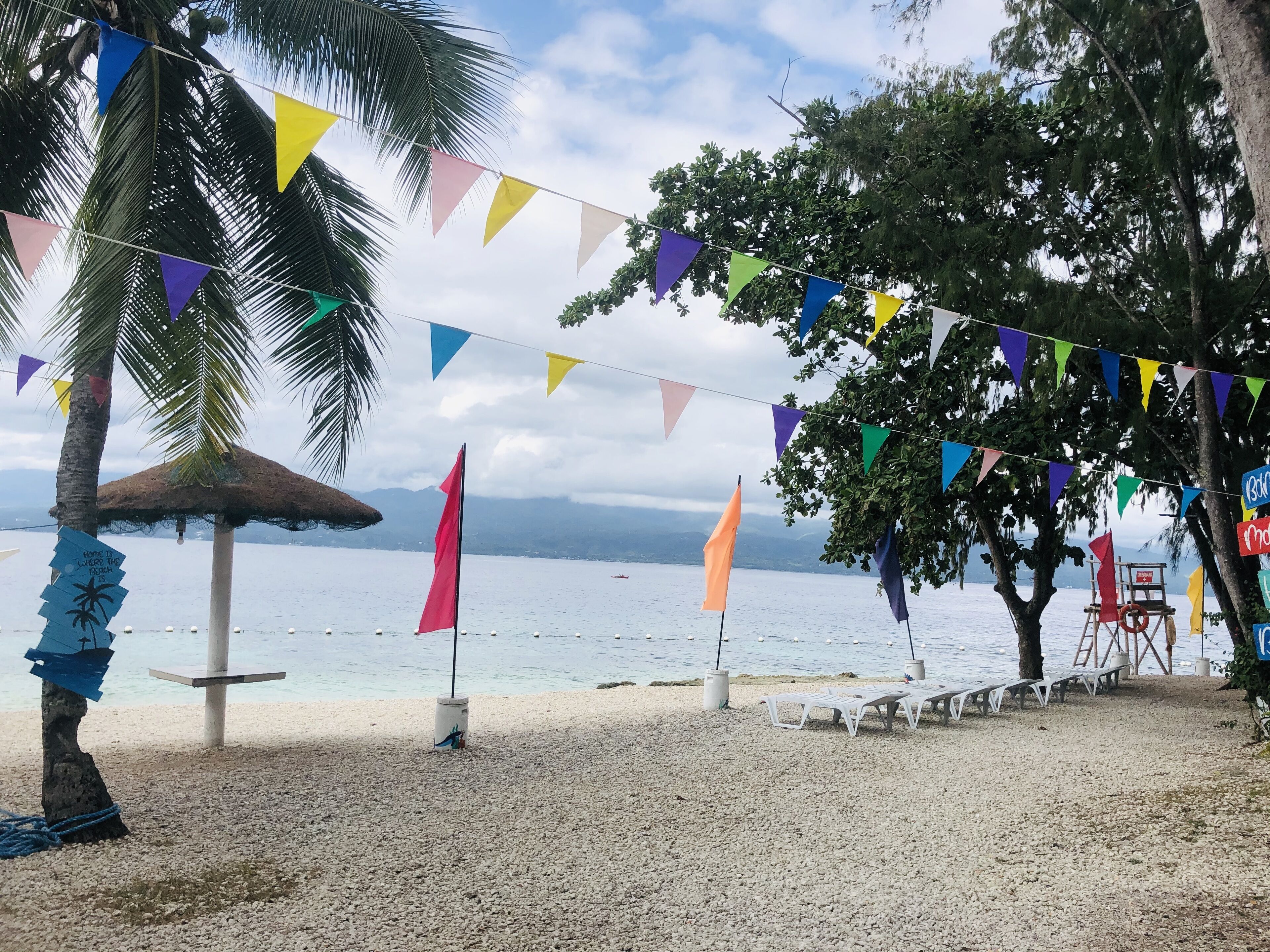 A beach with colorful triangular flags, a lifeguard tower, and a thatched umbrella.