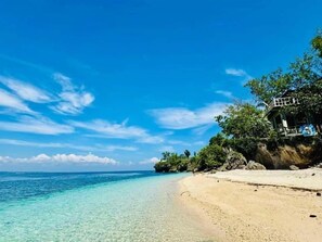 A beach with clear turquoise water, a sandy shore, and a building with a balcony overlooking the sea. - Santander Pebbles Beach Resort (Santander)