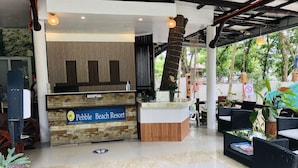 Un comptoir d’accueil portant l’inscription « Pebble Beach Resort », avec un décor en bois, un espace d’accueil doté d’un sol carrelé et un coin salon extérieur avec des meubles en osier.