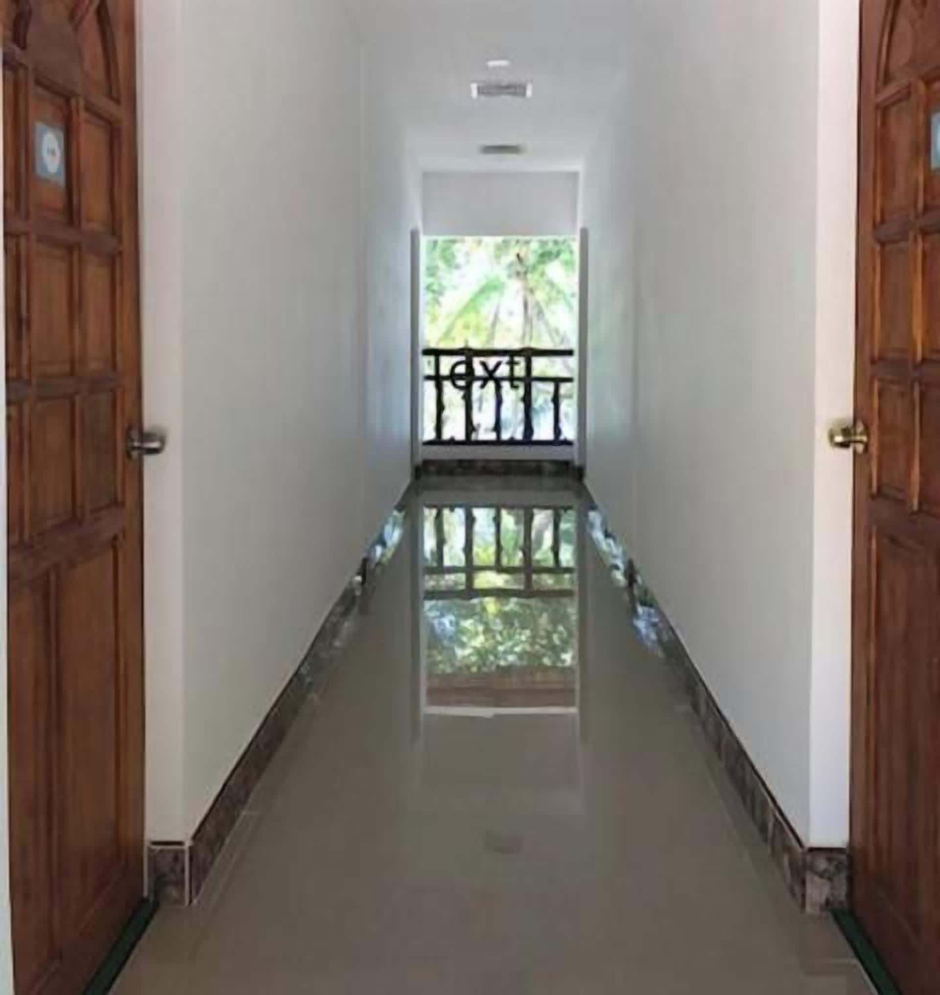 Corredor com portas de madeira de ambos os lados, dando acesso a uma varanda com guarda-corpo.