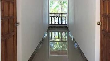 Corredor com portas de madeira de ambos os lados, dando acesso a uma varanda com guarda-corpo.
