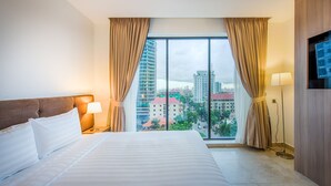 Habitación de hotel con una cama grande, dos lámparas de noche y vistas a la ciudad a través de ventanales del suelo al techo.