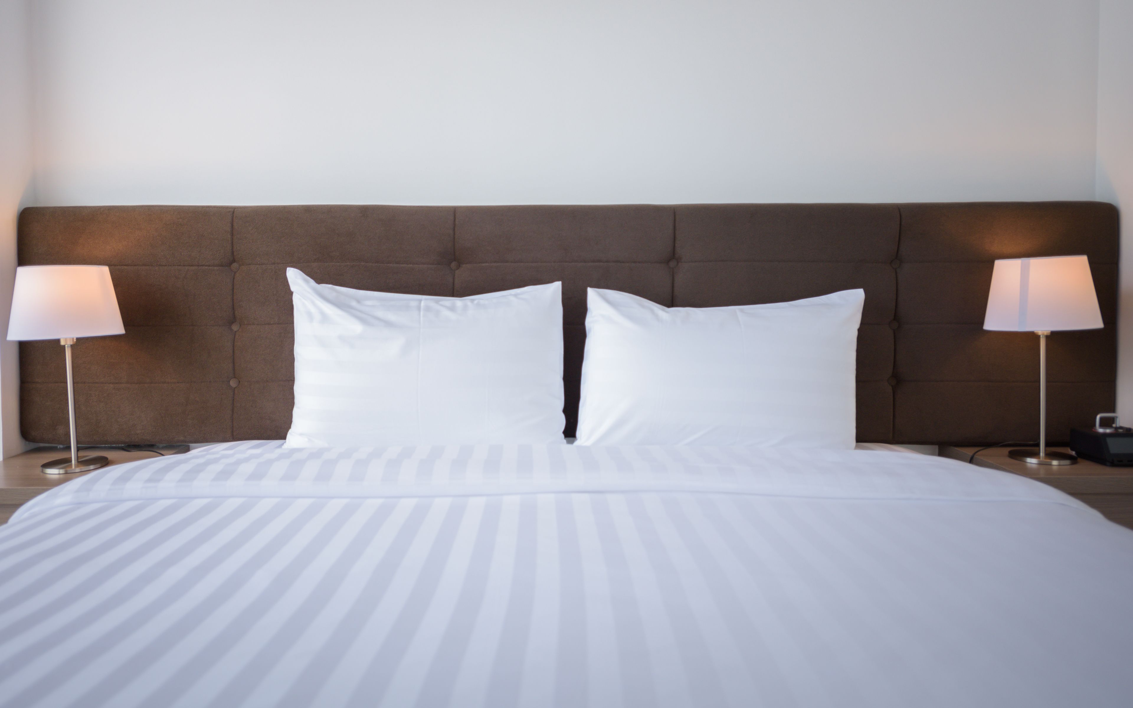 A neatly made bed with white bedding, a tufted headboard, and two bedside lamps on either side.