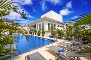 Un hotel con piscina, sillones de descanso y palmeras.
