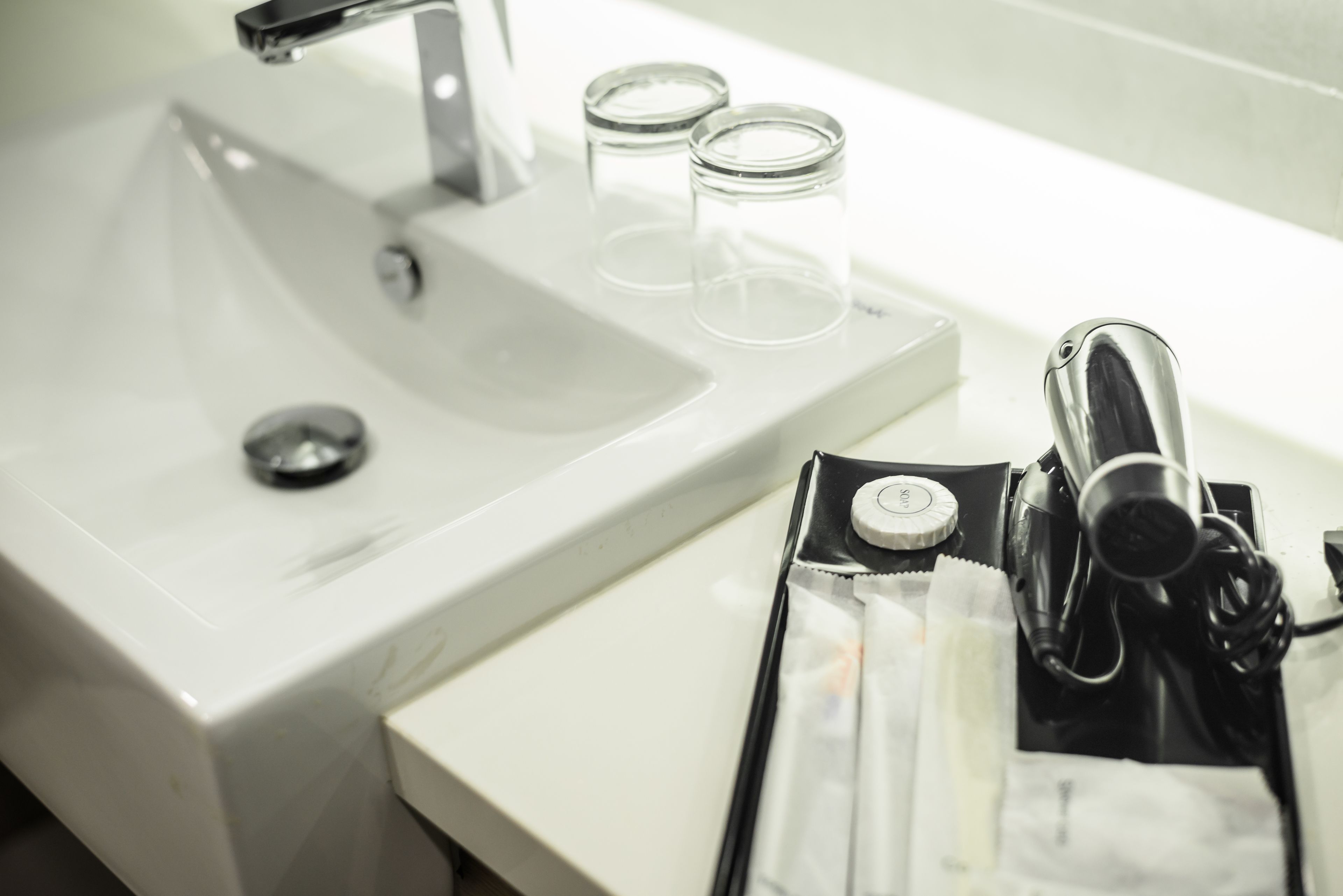 A bathroom sink with a mirror, two clear glasses, and a black toiletry bag with a bottle.