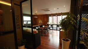 A hotel lobby with a wooden reception desk, a visible toilet sign, and a large potted plant. - Noel Business Hotel (Busan)