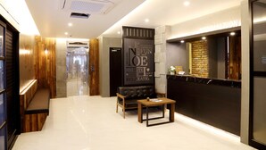 A modern hotel lobby with a reception desk, a seating area, and a glass door leading to a bathroom. - Noel Business Hotel (Busan)