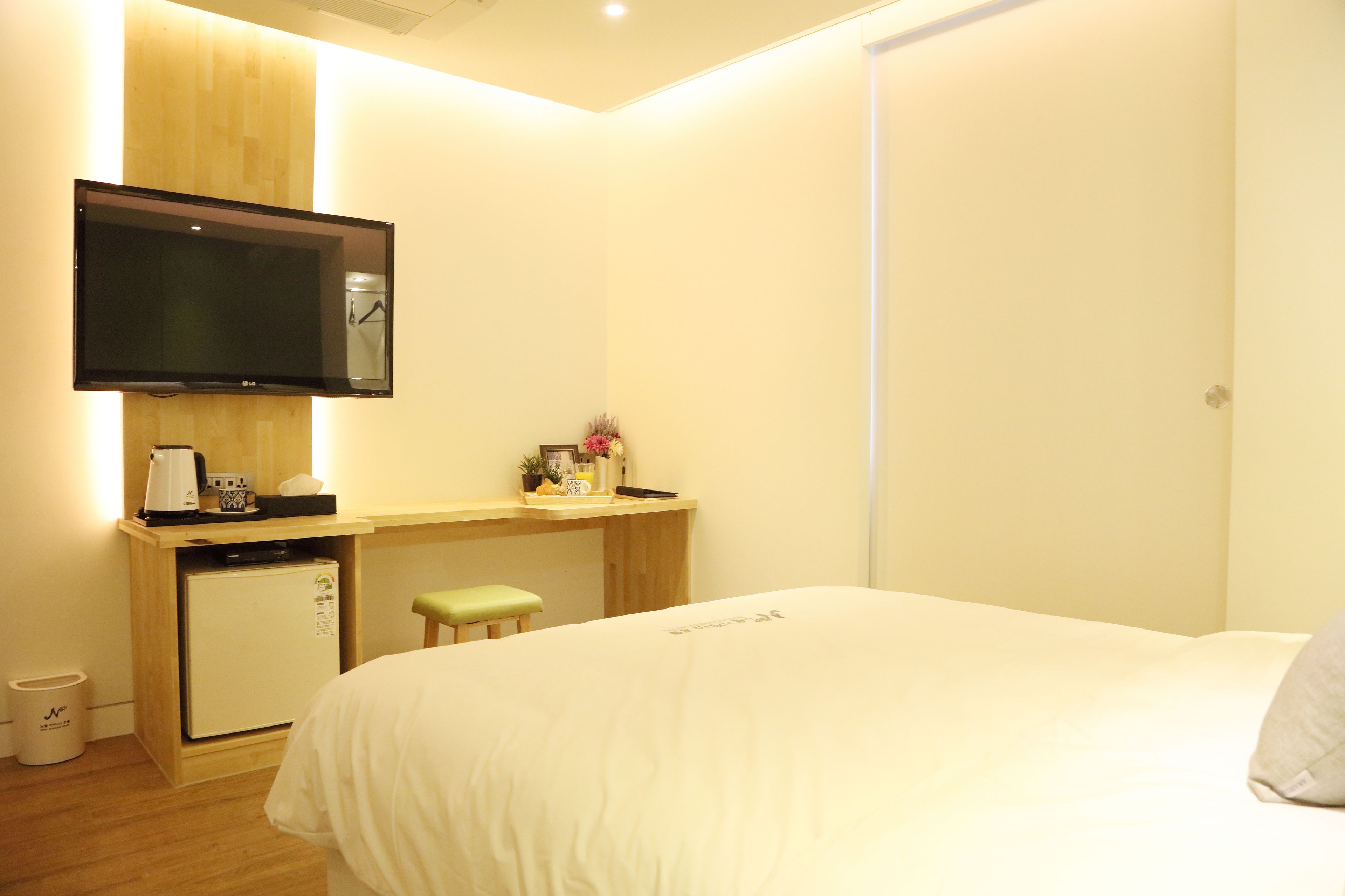 A hotel room with a bed, a desk with a computer, a television, and a small refrigerator.