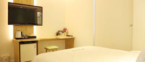 A hotel room with a bed, a desk with a computer, a television, and a small refrigerator.
