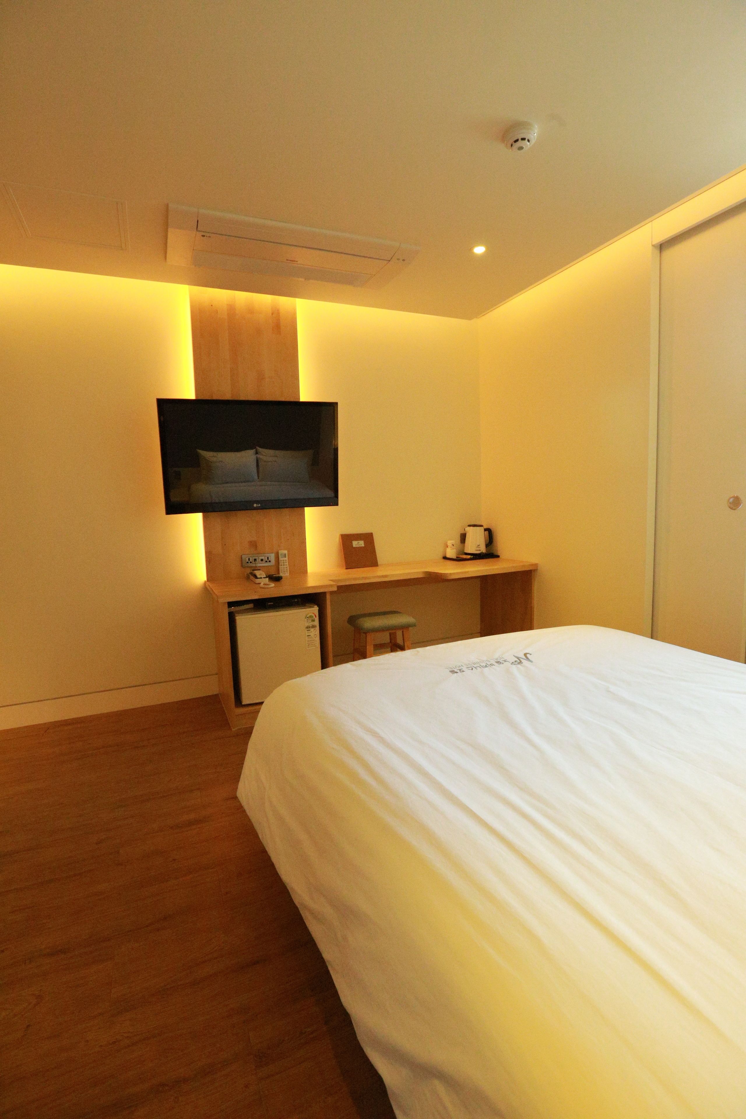 Una habitación de hotel con cama, escritorio, televisión en la pared y un refrigerador pequeño.