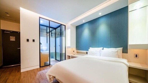 A modern hotel room with a large bed, a glass door leading to a balcony, and a dark blue accent wall. - Noel Business Hotel (Busan)