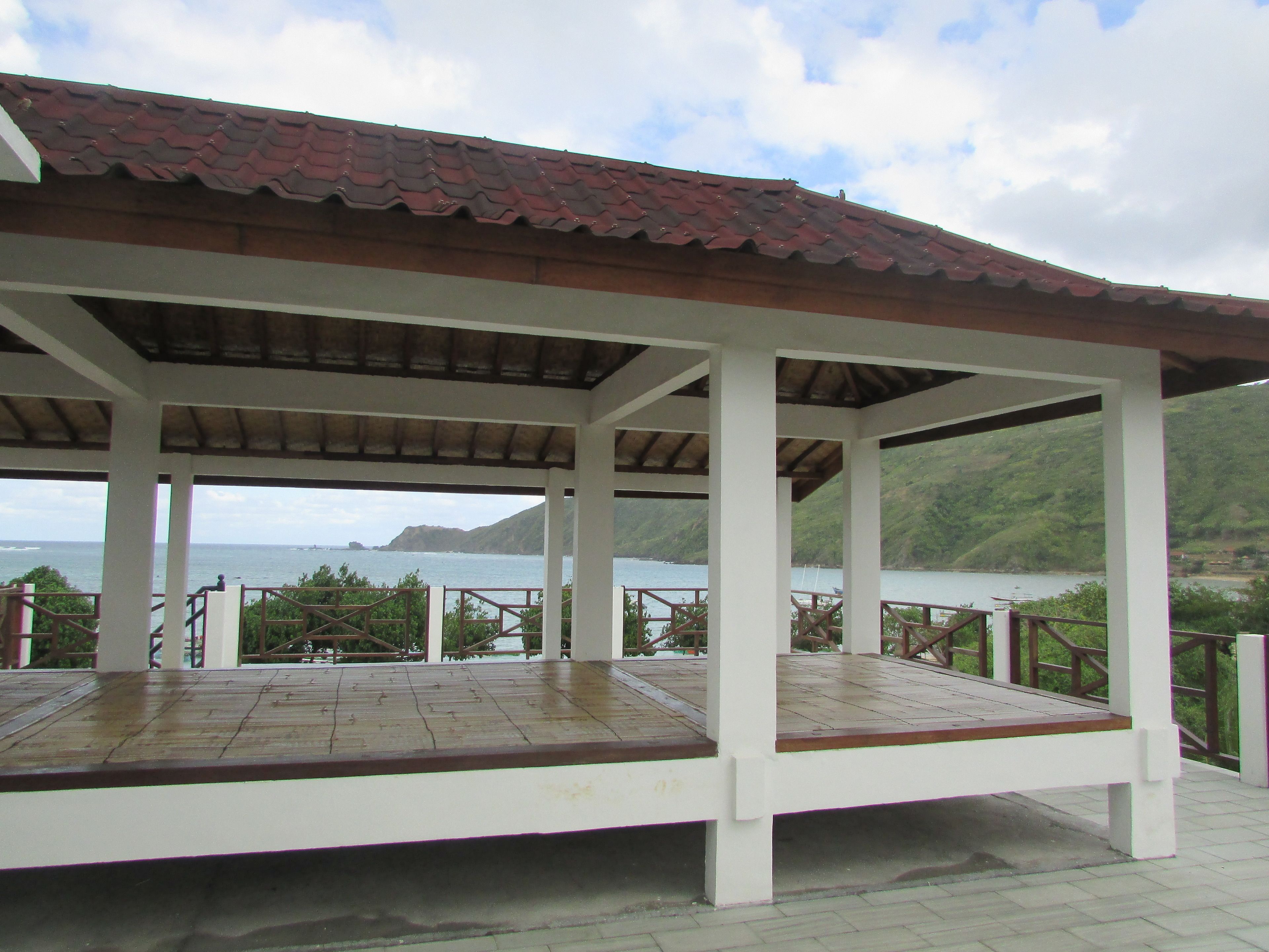 A covered outdoor area with a view of the sea and hills.