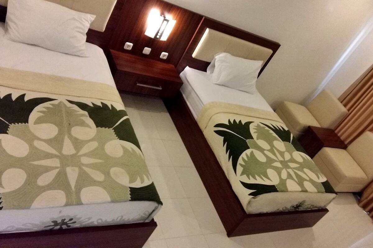 A hotel room with two beds, each with a floral bedspread, a nightstand with a lamp, and a sofa.