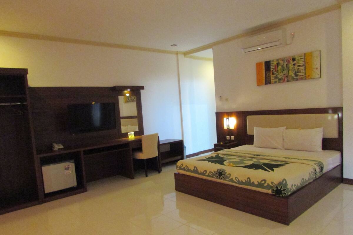 A hotel room with a bed, a desk, a television, and a small seating area.