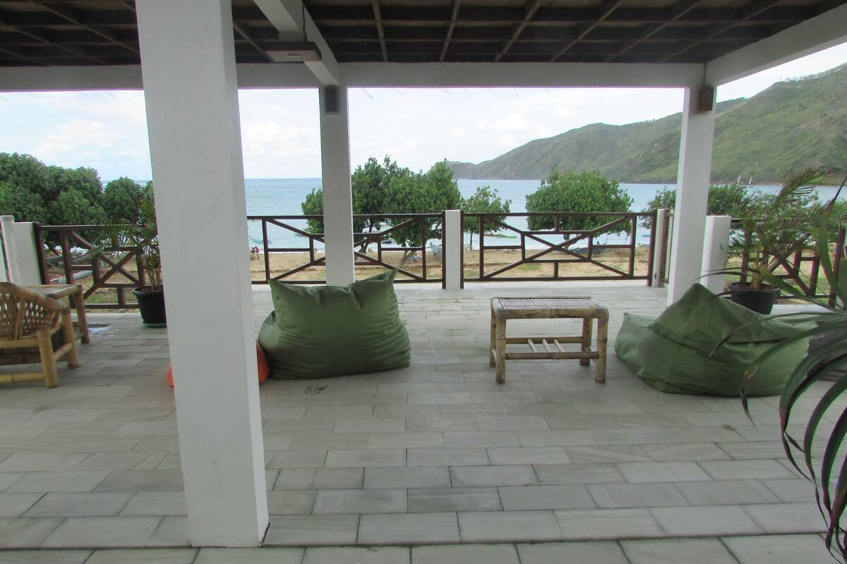 A covered outdoor seating area with a view of the sea and hills.