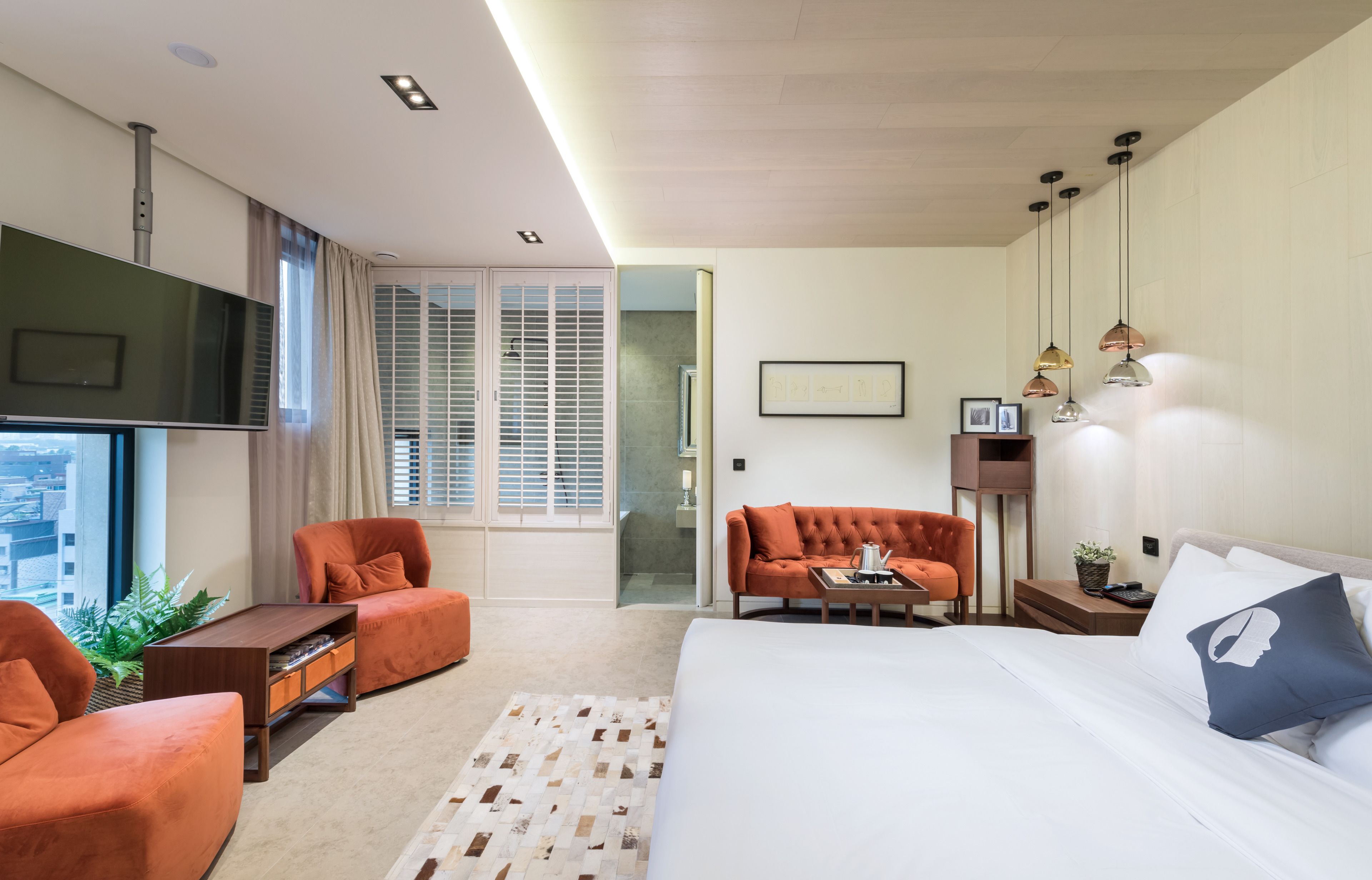 A hotel room with a large bed, two orange armchairs, a sofa, a TV, and a city view.