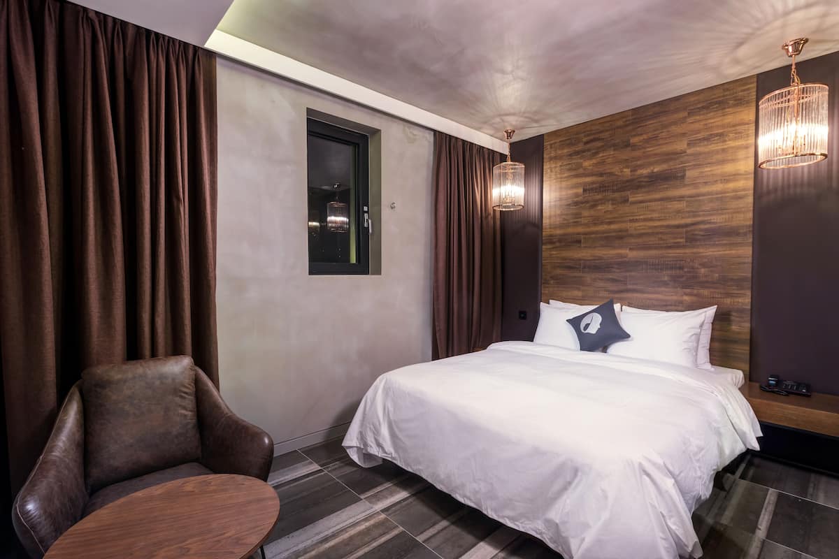 A modern hotel room with a large bed, a leather armchair, and a small table.