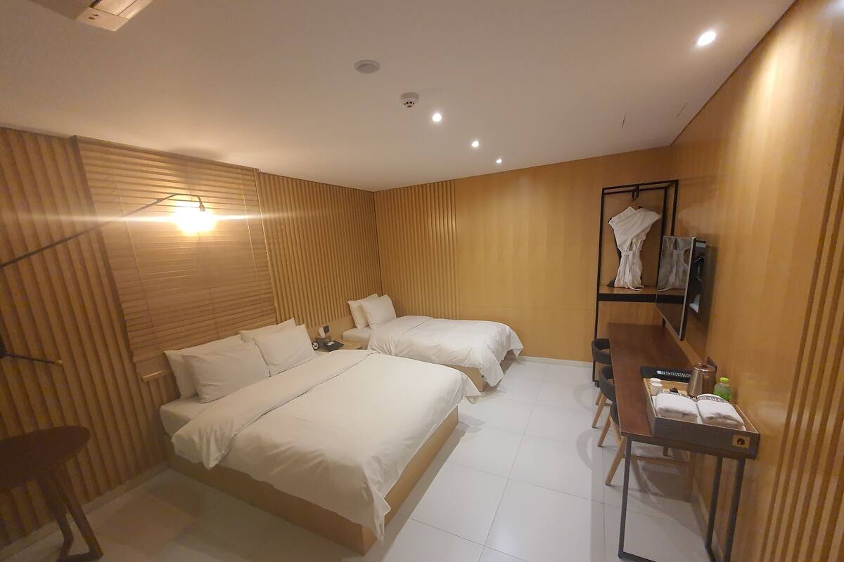 A hotel room with two beds, a desk with a chair, a TV, and a coat rack.