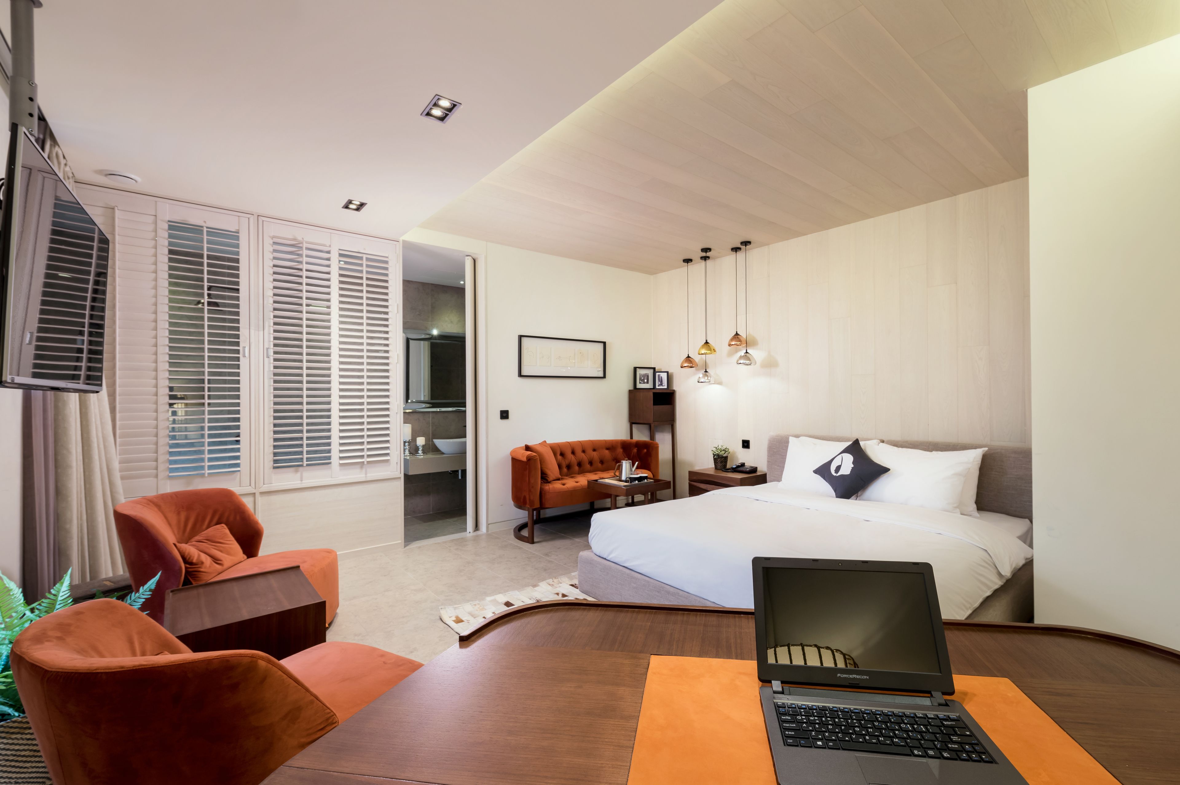 Una habitación de hotel moderna con una cama grande, un escritorio con una computadora portátil, un sofá y un comedor.