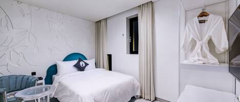 Habitación de hotel moderna con una cama, una mesa redonda, un sillón azul y una bata colgada en un perchero.