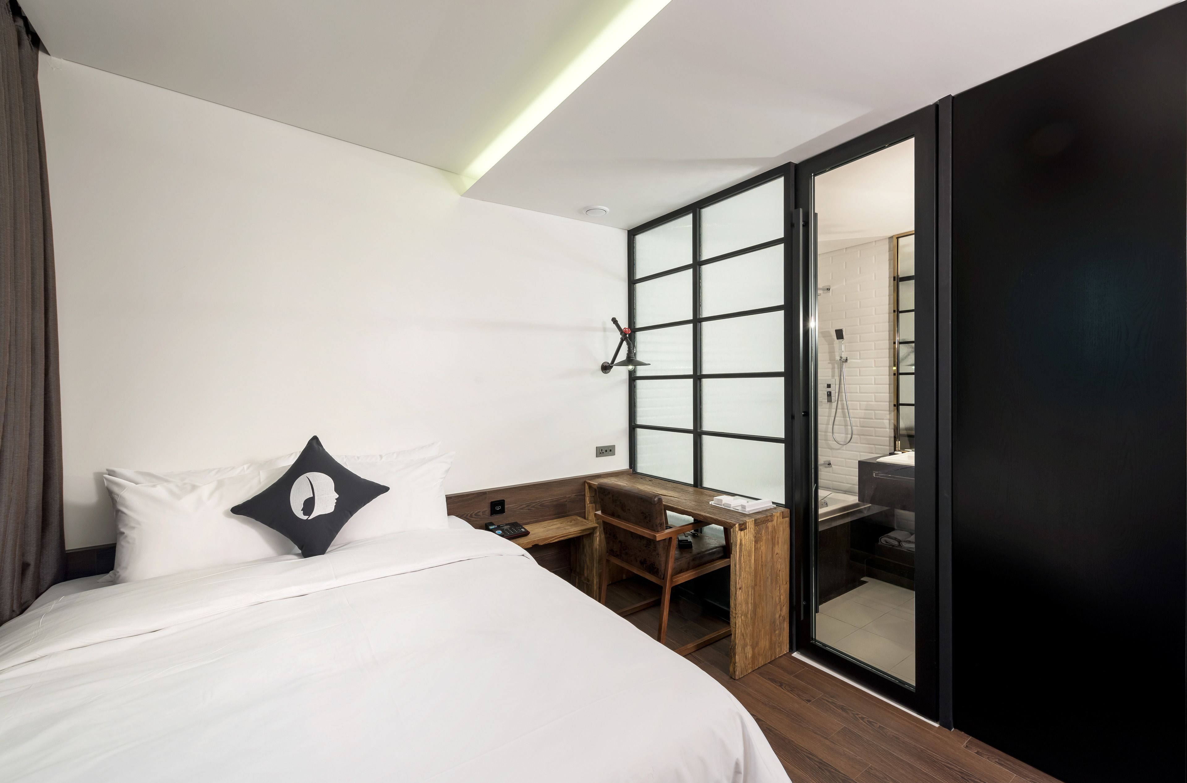 A modern hotel room with a bed, a desk, and a sliding door leading to a bathroom.