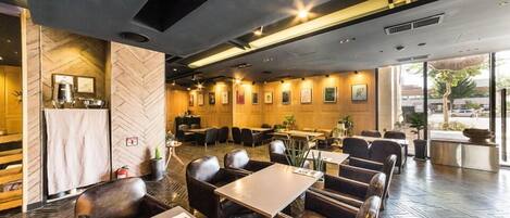 A restaurant with a modern interior, featuring a mix of seating arrangements including booths and tables, a herringbone-patterned wall, and a view of the outdoors through large windows.