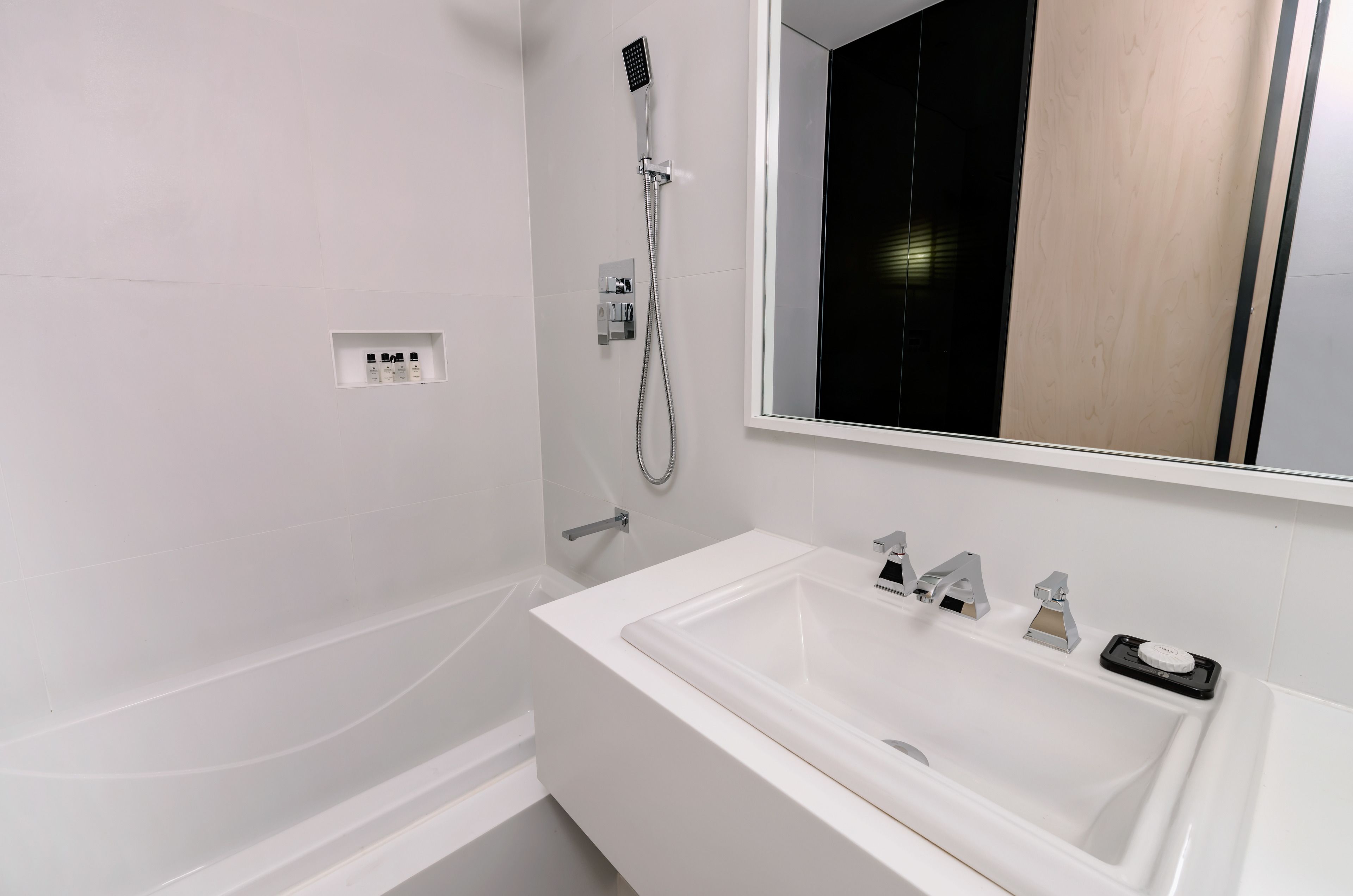 Une salle de bain moderne avec une baignoire blanche, un grand miroir et une pomme de douche.