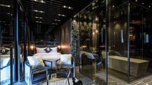 Habitación de hotel moderna con una cama grande, un sofá, un baño con paredes de vidrio y una figurita de perro sobre la alfombra.
