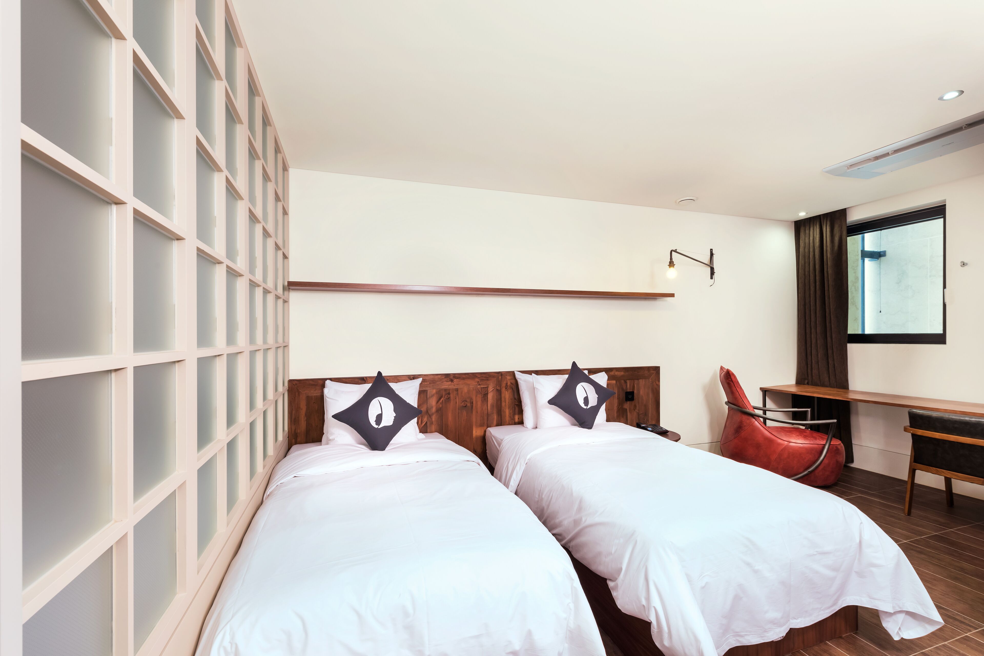 A hotel room with two single beds, a desk, a chair, and a large window.