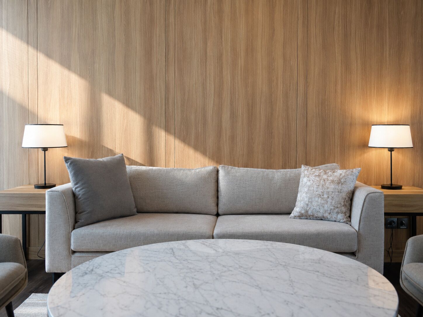 Una sala de estar moderna con un sofá curvo, dos mesitas de noche con lámparas y una mesa de centro de mármol.