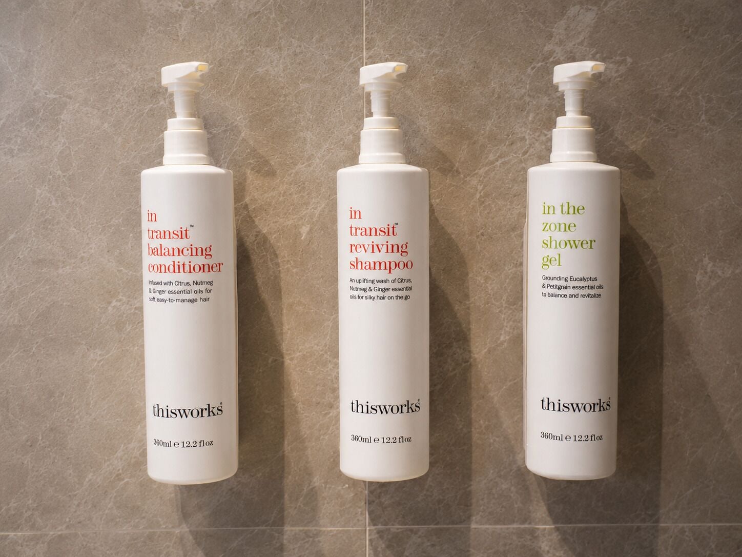 Trois bouteilles de shampooing de la marque thisworks posées sur une surface carrelée.