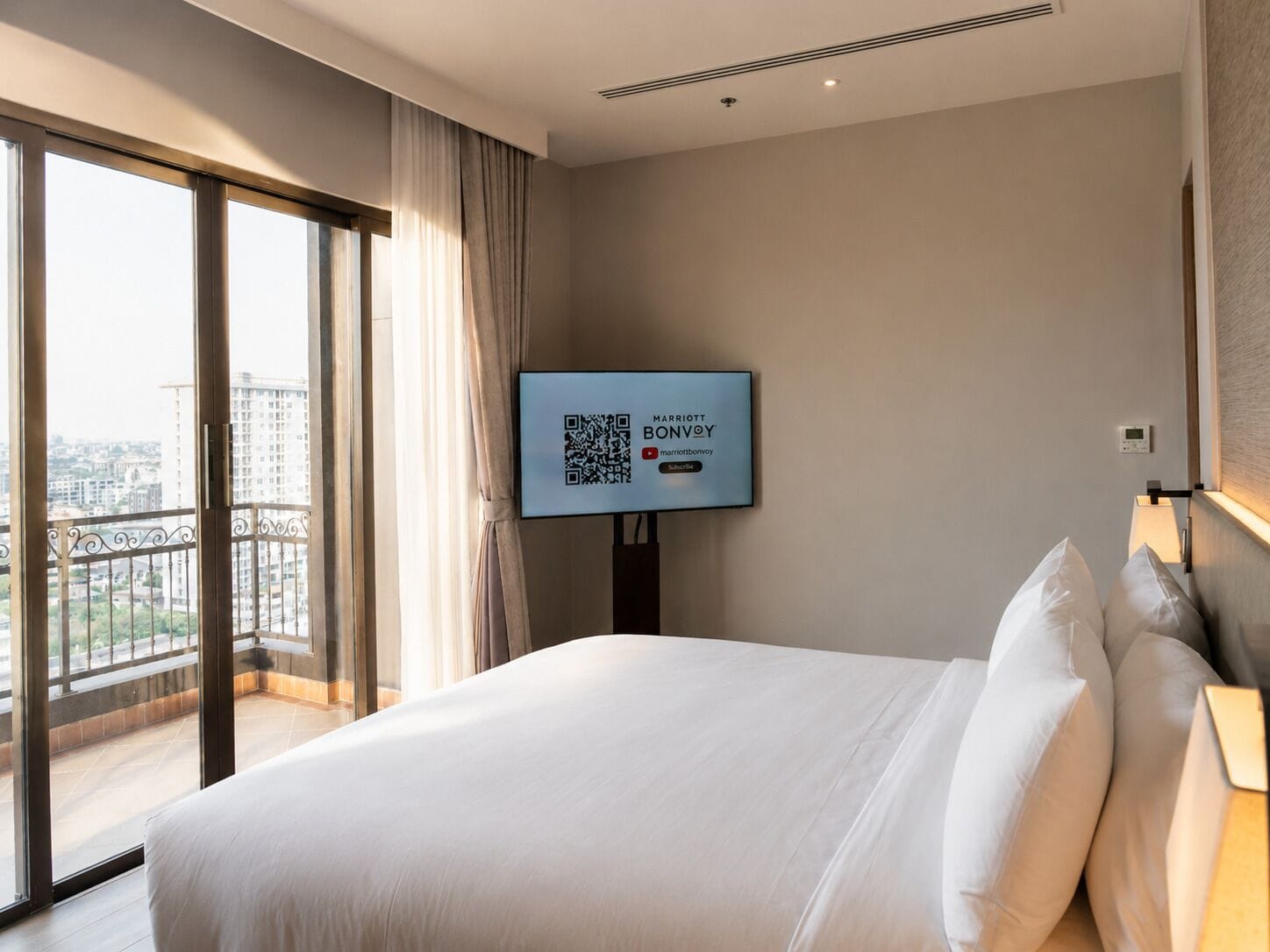 A hotel room with a large bed, a television mounted on the wall, and a view of the city through a large window.