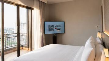 A hotel room with a large bed, a television mounted on the wall, and a view of the city through a large window.