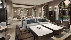 Un hall d’hôtel moderne avec des espaces de détente, une vue sur la piscine et un coin repas.
