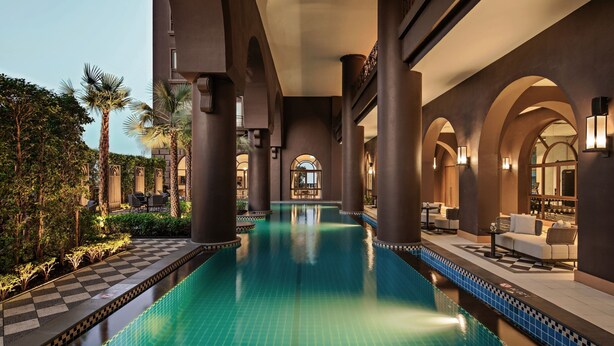 Un área de piscina con suelo a cuadros, palmeras y mobiliario de relax.