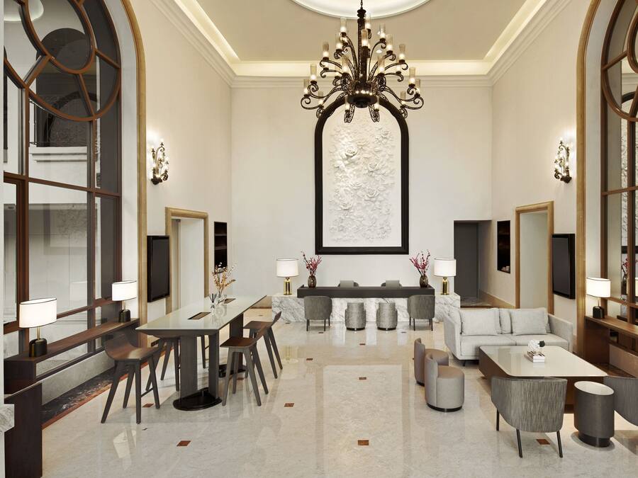 A spacious lobby with a grand chandelier, a reception desk, seating area, and a large decorative wall.