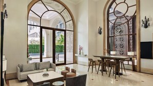 Un amplio lobby con sofá, mesa de centro y zona de comedor, con ventanas arqueadas grandes y paneles decorativos en las paredes.