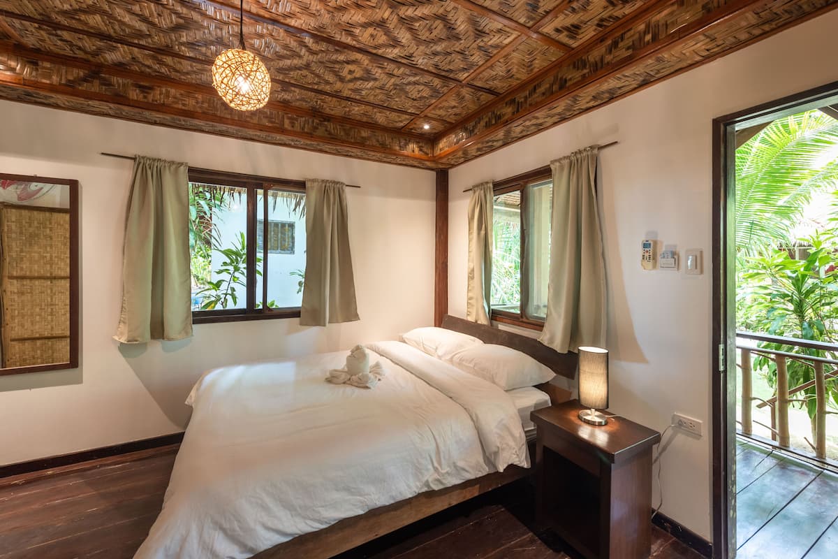 Une chambre avec un plafond en bois, un lit recouvert de draps blancs et une table de chevet avec une lampe.